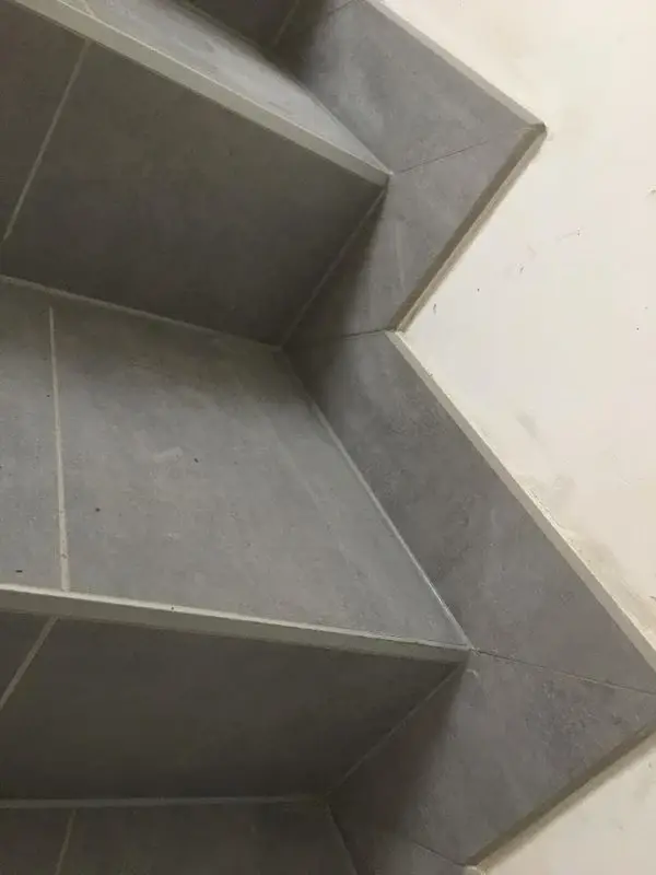 Vue en contre-plongée d’un escalier intérieur carrelé avec précision, utilisant des carreaux gris effet béton.