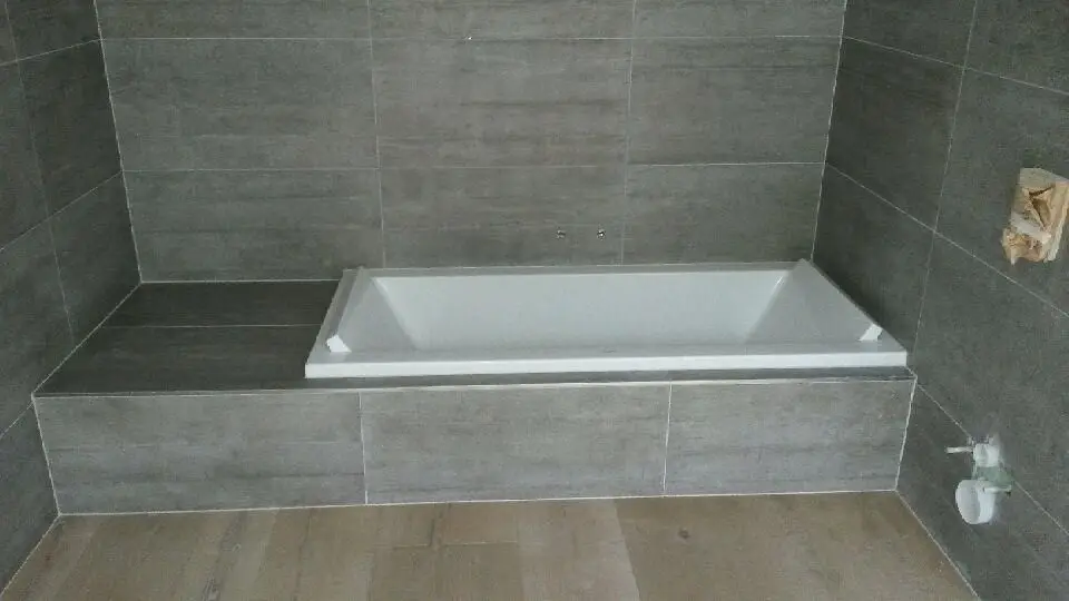 Baignoire encastrée dans une salle de bain moderne, entourée de carrelage gris anthracite et sol en bois clair.