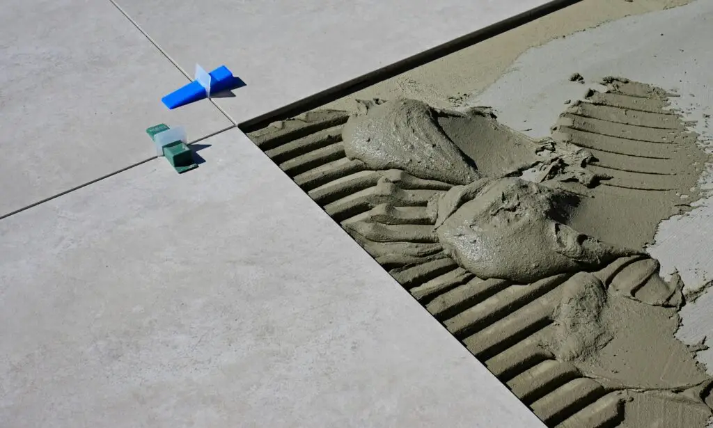 Gros plan sur le ciment humide et les cales de carrelage lors de la pose de carreaux de sol représentant la marque Pro Chape Carrelage.
